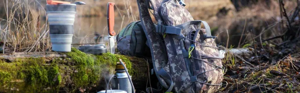 Image of an outdoors scenario with cooking tools, knife, and backpack.