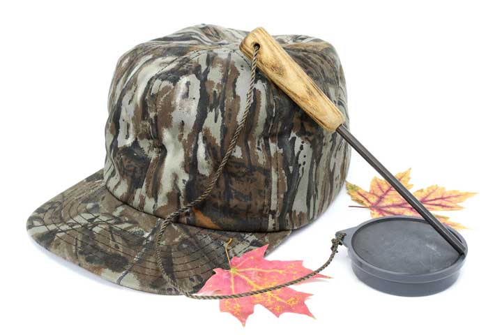 Photo of a turkey pot call and a camouflage hat. 
