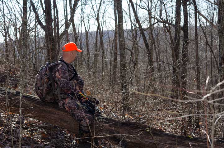 Photo of an archery deer hunter sitting on a log, waiting for the deer. 