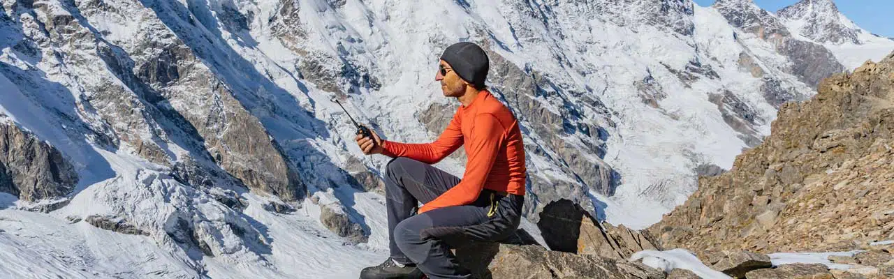 Photo of a man holding an emergency radio, waiting to be rescued in the mountains.