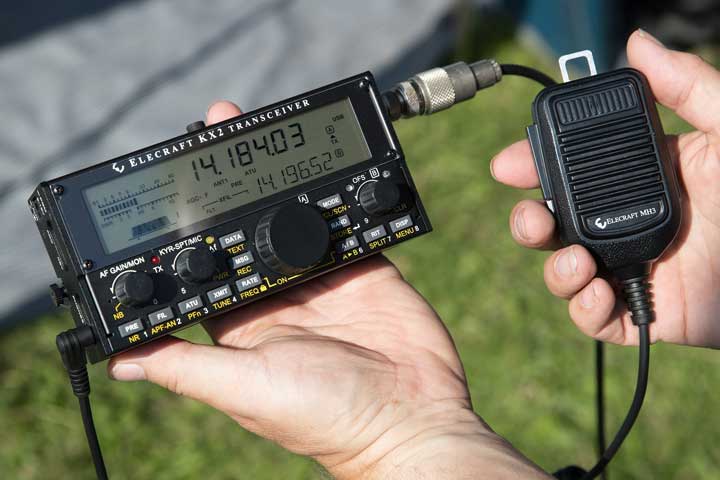 Photo of an emergency radio held in one hand, while the other hand holds the microphone. 