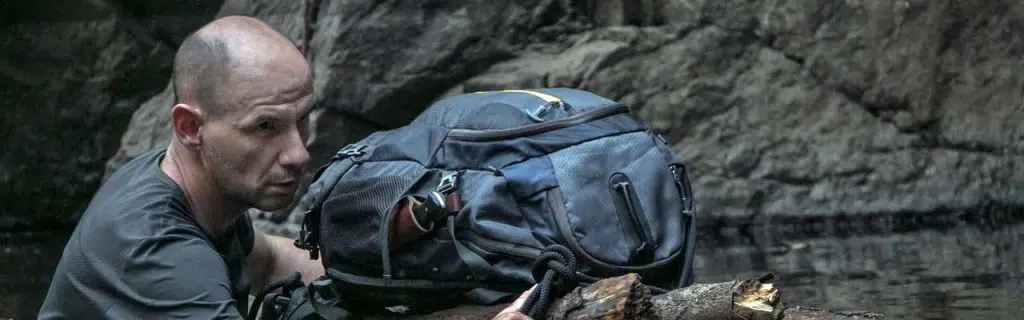 Photo of a survivalist crossing a river protecting his backpack on a floating log.