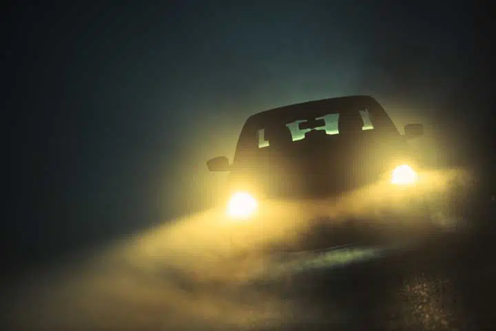 Photo of a car with the lights on on a dark, foggy night.