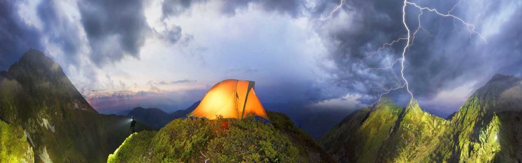 Photo of a tent in the peak of a mountain during a thunderstorm.