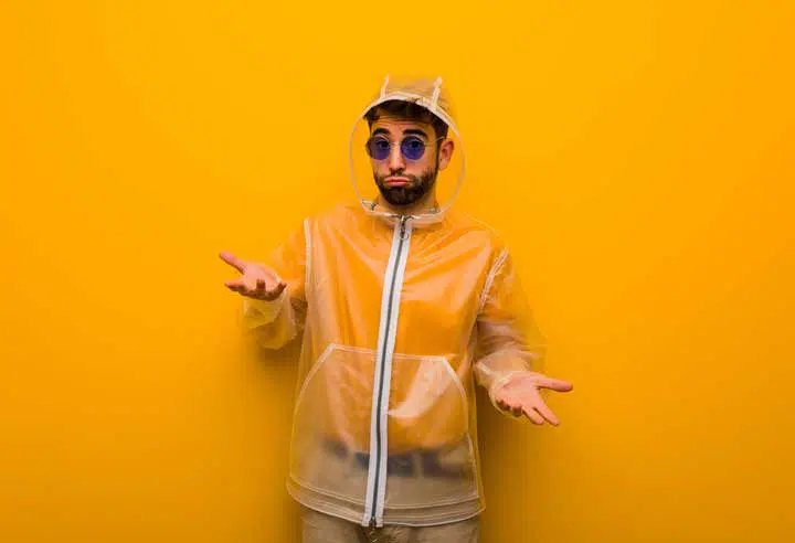 Young man wearing a rain coat confused and doubtful. 