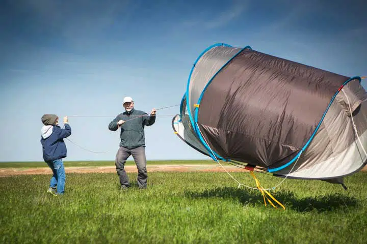 A boy and a man trying to hold a tent about to fly away because of the wind. 