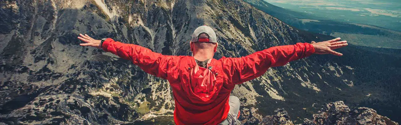 A hiker in outdoor red windbreaker jacket enjoys the magnificent view sitting on the edge of precipice in the Tatra Mountains in Slovakia.