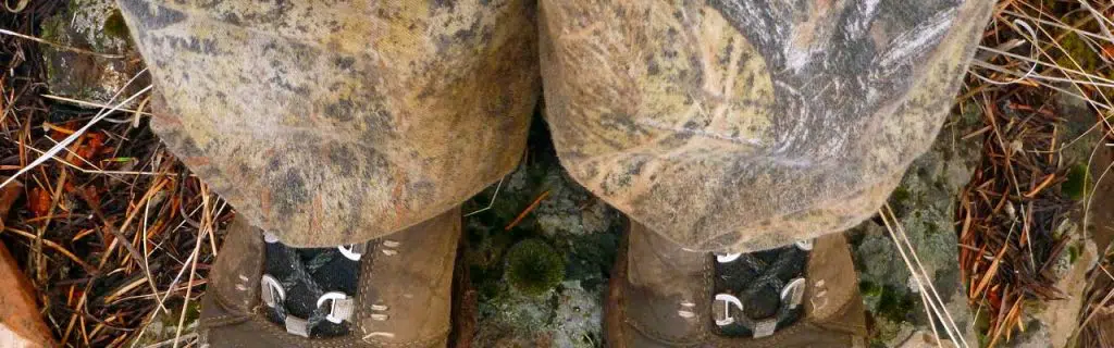 A hiker looking down at her hunting boots while standing on a rock while wearing camouflaged pants.