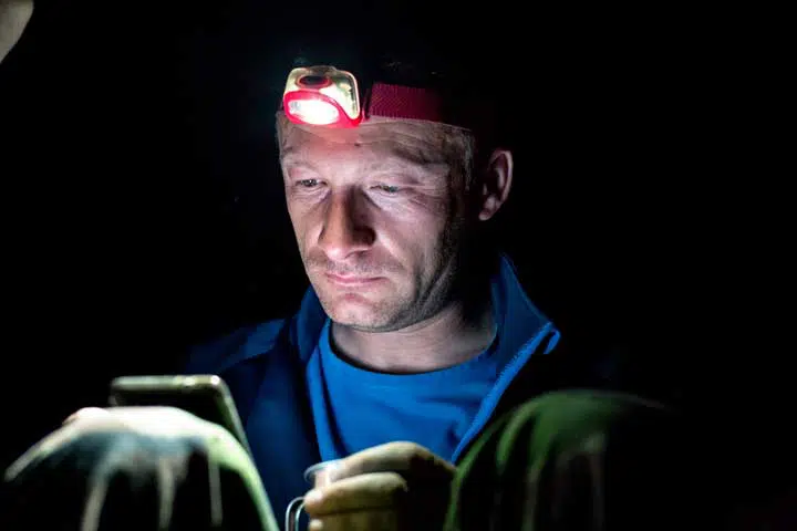 camping outdoors in nature on open sky at night , explorer is texting and using phone. 