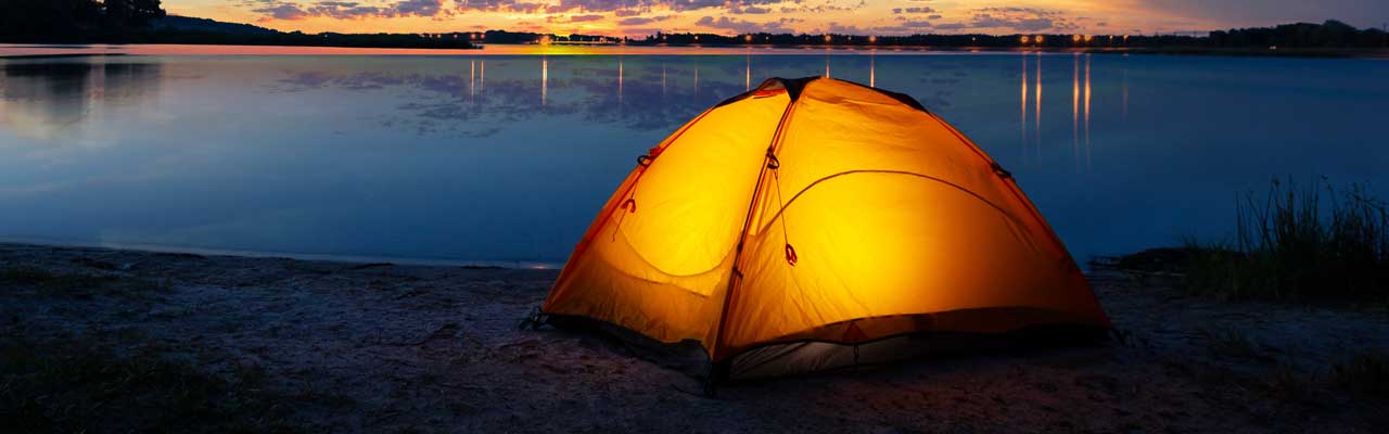 Orange tourist lit tent by the lake at sunset.