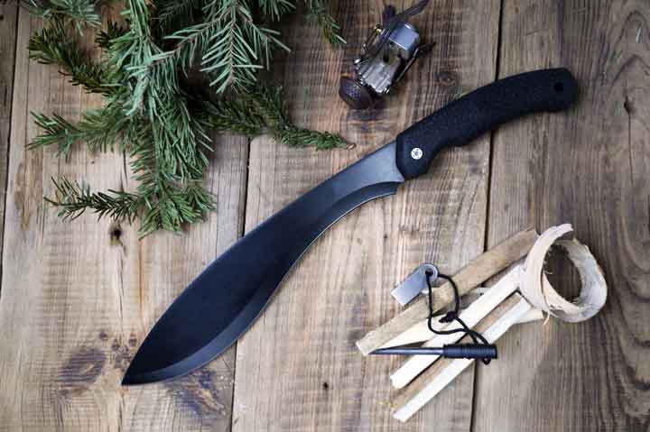 Kukri machete on wooden background and coniferous branches. Machete top view. Flat lay.
