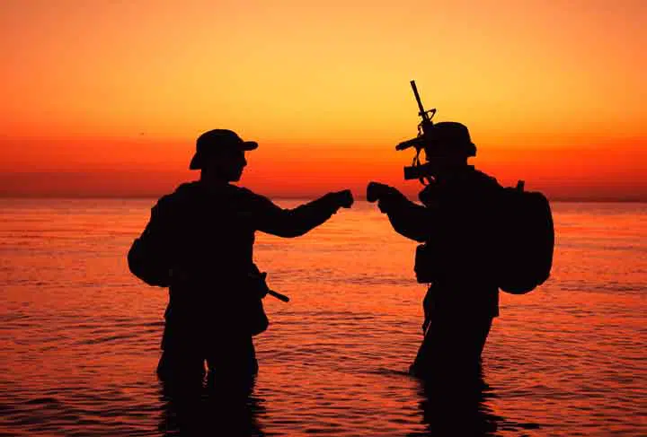 Army special operations forces soldiers, commando fighters doing fist dump gesture while standing knee-deep in water.