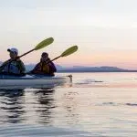 Group of people friends sea kayaking together at sunset in beautiful nature.