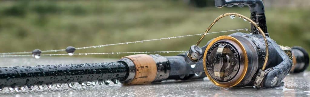 The fishing rod with the reel lies in the rain. Drops of water hang from the fishing rod.