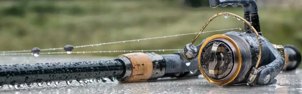 The fishing rod with the reel lies in the rain. Drops of water hang from the fishing rod.