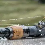 The fishing rod with the reel lies in the rain. Drops of water hang from the fishing rod.