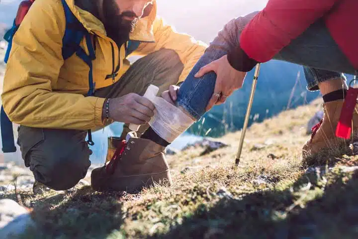 A woman has sprained her ankle while hiking, her friend uses the first aid kit to tend to the injury. 