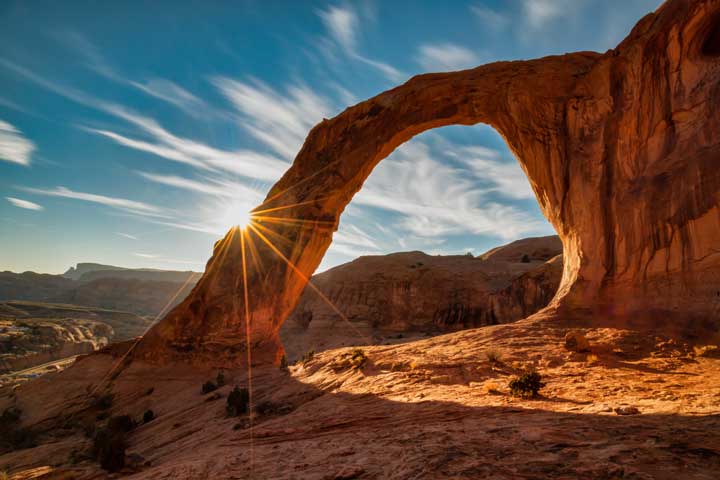 An image of Corona Arch in Utah with a sunburst