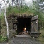 Photo of a bushcraft shelter with fireplace inside, in the middle of the woodlands.